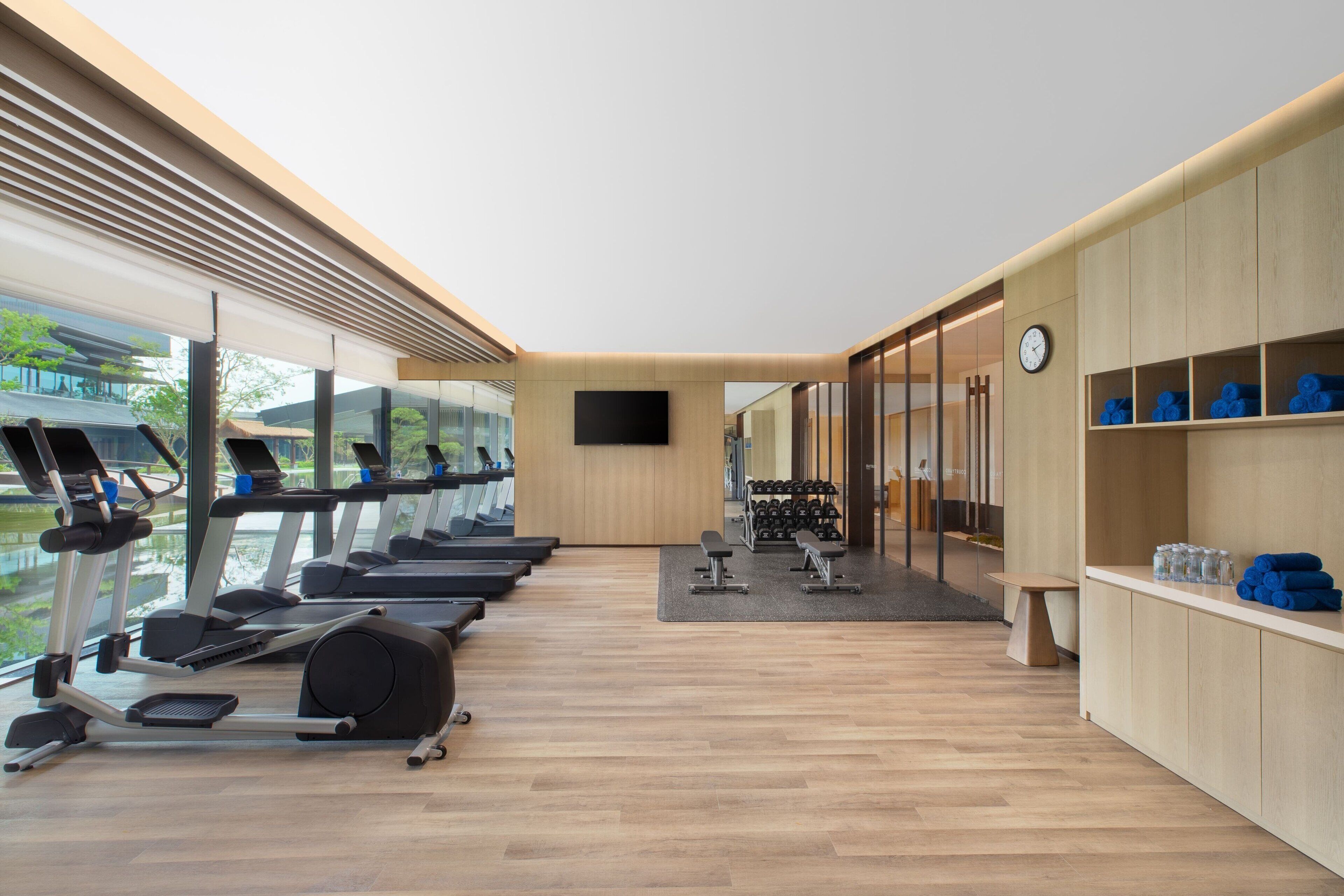 Un gimnasio moderno con cintas de correr, pesas y un ventanal que da a zonas verdes.