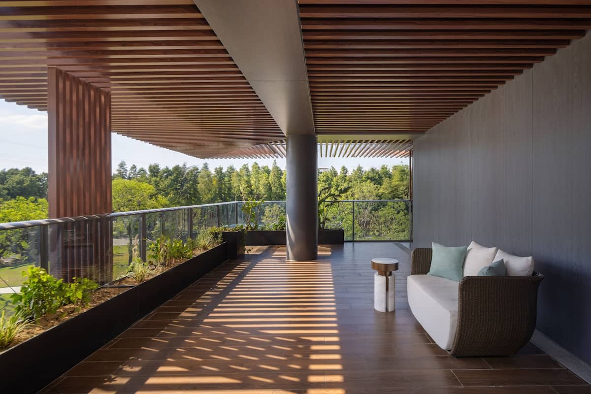 Un balcon moderne doté d’un plafond en bois, d’un espace salon avec des coussins et offrant une vue sur un paysage boisé.
