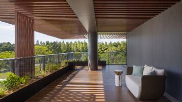 Un balcón moderno con techo de madera, un área de descanso con cojines y vistas a un paisaje boscoso.
