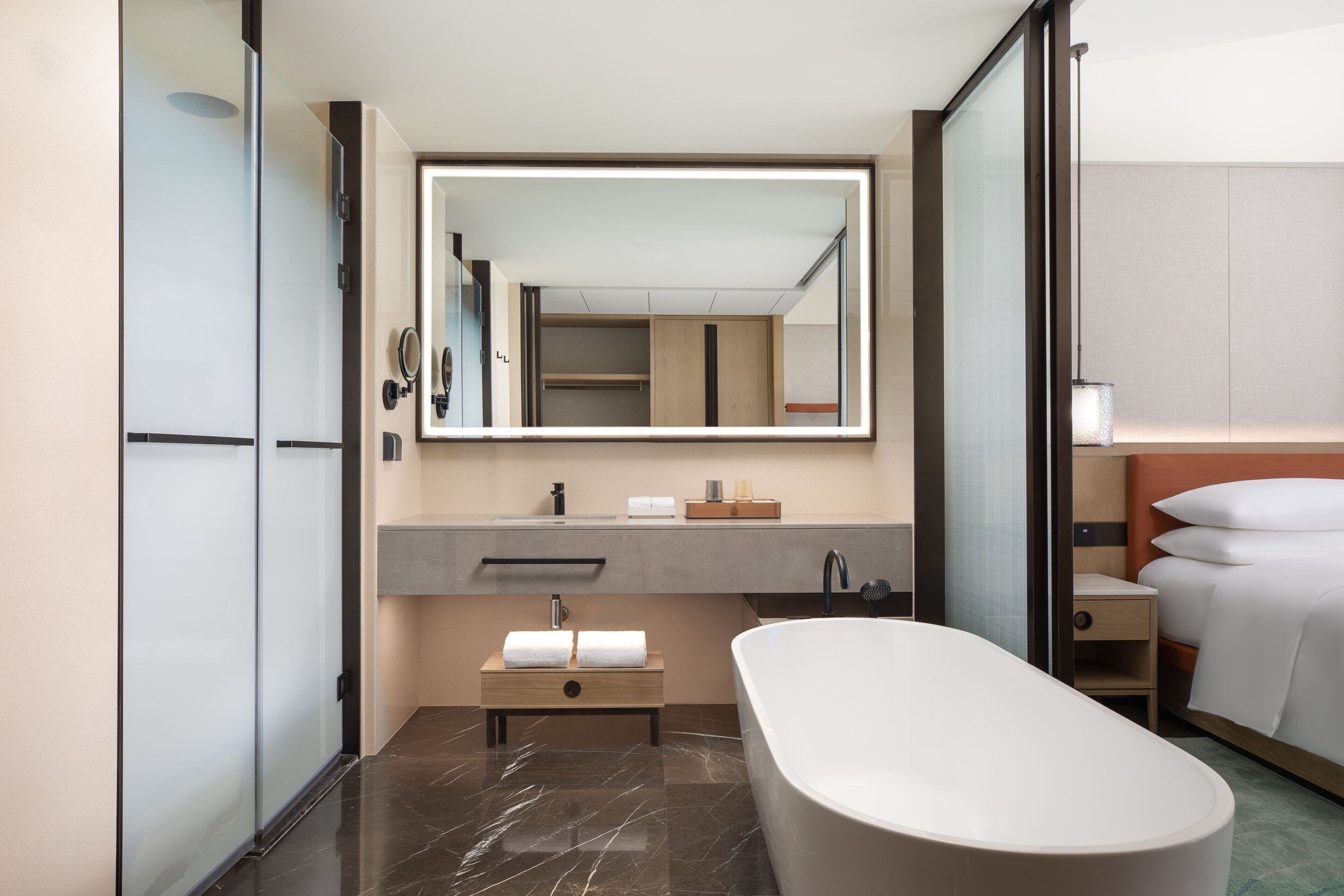 Une salle de bain moderne avec une baignoire sur pieds, un grand miroir, un meuble-lavabo et une table de chevet avec une lampe.