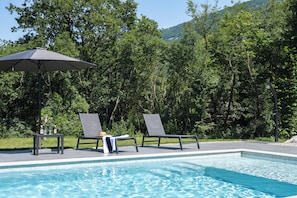 A pool area with two lounge chairs, a table with bottles, and an umbrella.