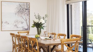 A dining area with a wooden table, six chairs, a vase with flowers, and a framed painting on the wall.