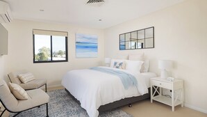 A bedroom with a bed, a chair, a nightstand, a window, and a painting.
