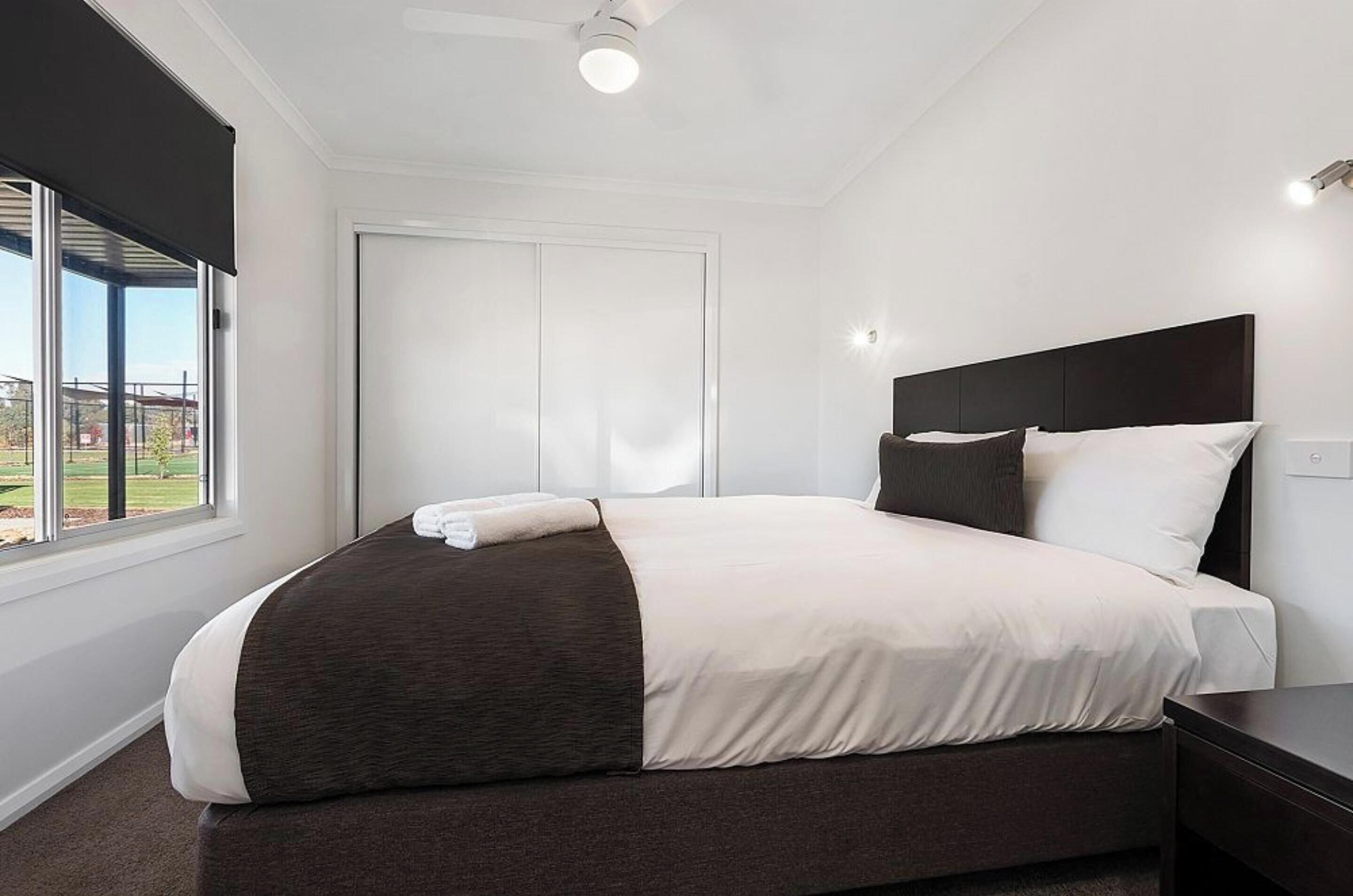 Een moderne hotelkamer met een groot bed, een donker hoofdbord, een nachtkastje en een raam met uitzicht op een gebouw en groen.