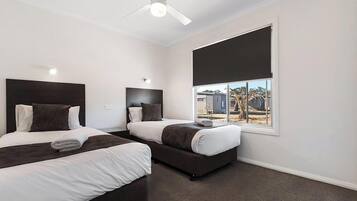 A hotel room with two beds, a ceiling fan, a large window with a view of the outside, and a dark-colored carpet.