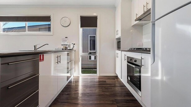 A modern kitchen with white cabinets, stainless steel appliances, and a wooden floor. - Discovery Parks Moama Waters  (Moama)