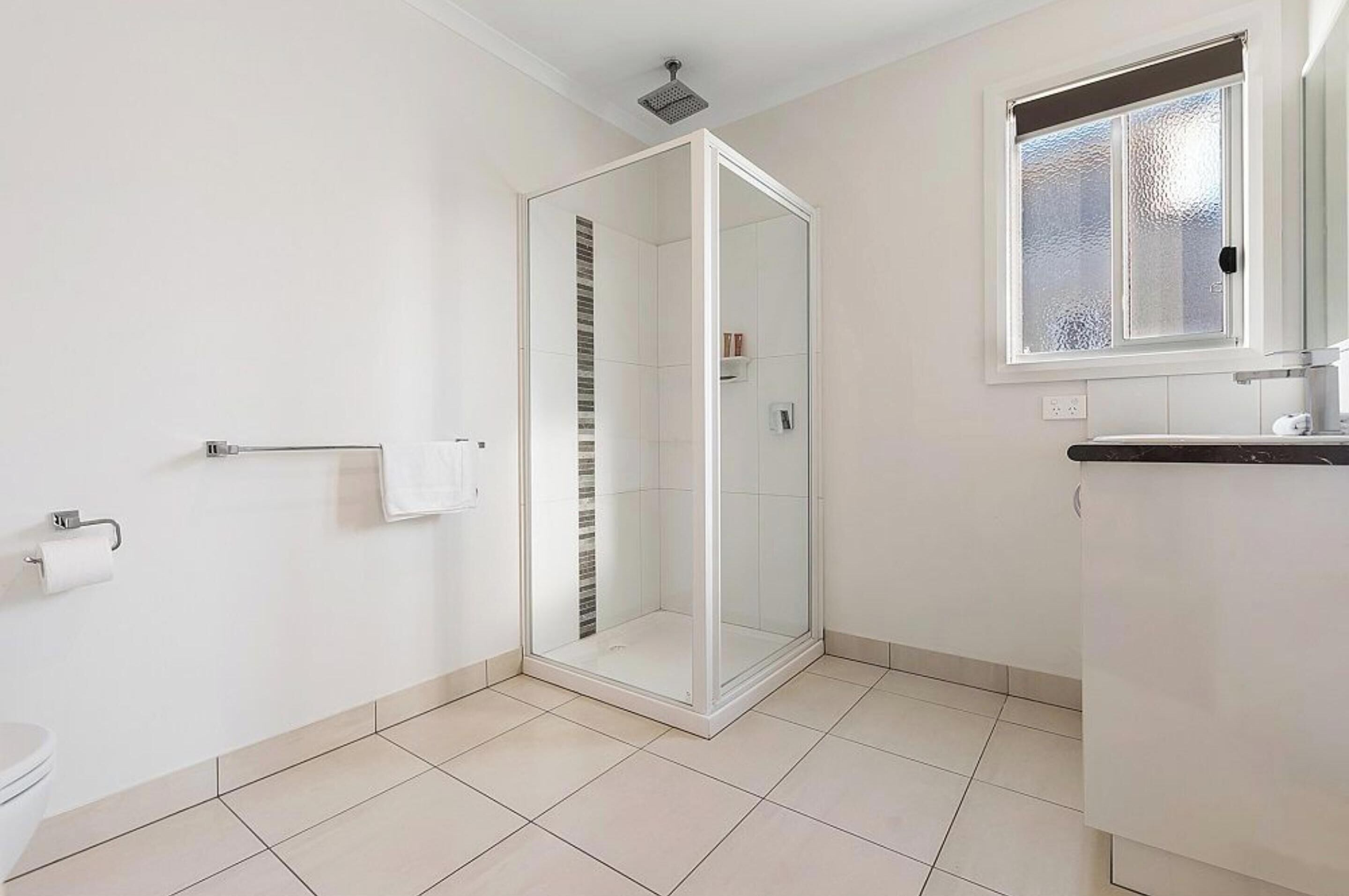 A modern bathroom with a glass shower enclosure, a toilet, a towel rack, and a window with frosted glass.