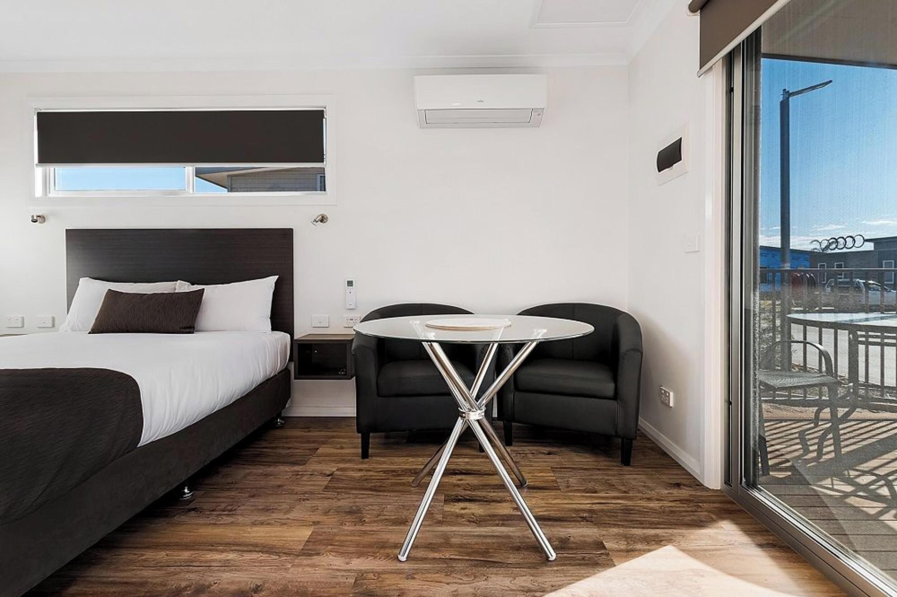 Quarto de hotel moderno com uma cama grande, uma mesa redonda pequena, um sofá e uma varanda com mobiliário de exterior.
