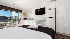 A modern hotel room with a large bed, a balcony with a view, a kitchenette, and a flat-screen TV. - Discovery Parks Moama Waters  (Moama)