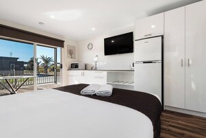 Una habitación de hotel moderna con una cama grande, un balcón con vistas, una kitchenette y un televisor de pantalla plana.