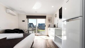 A modern hotel room with a bed, a kitchenette, a balcony with a view of buildings, and a flat-screen TV mounted on the wall. - Discovery Parks Moama Waters  (Moama)