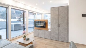 A modern living room with a fireplace, large sliding glass doors, and a view of a snowy landscape. - Penthäuser -Lorenzerhof Sauna (Murau)