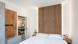 A modern bedroom with a large bed, wooden panel wall, and a small desk area. - Penthäuser -Lorenzerhof Sauna (Murau)