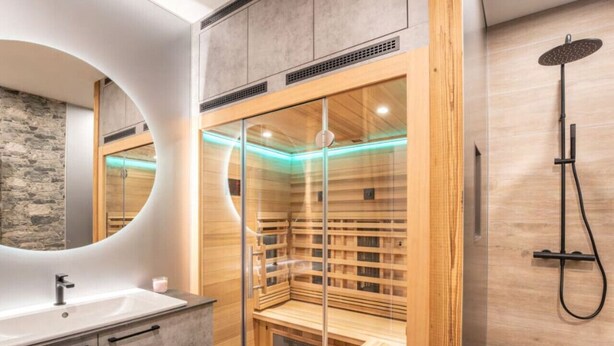 A modern bathroom with a large mirror, a wooden sauna, and a shower. - Penthäuser -Lorenzerhof Sauna (Murau)