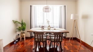 Un coin repas comprenant une table en bois, quatre chaises, un luminaire suspendu, une plante en pot et une lampe sur pied.