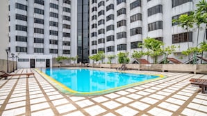 Une piscine dotée d’une plage carrelée, entourée d’un immeuble de grande hauteur comportant de nombreux étages et balcons.
