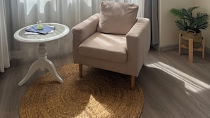 Un salon moderne avec un fauteuil beige, une petite table ronde ornée d’un vase et une plante en pot.