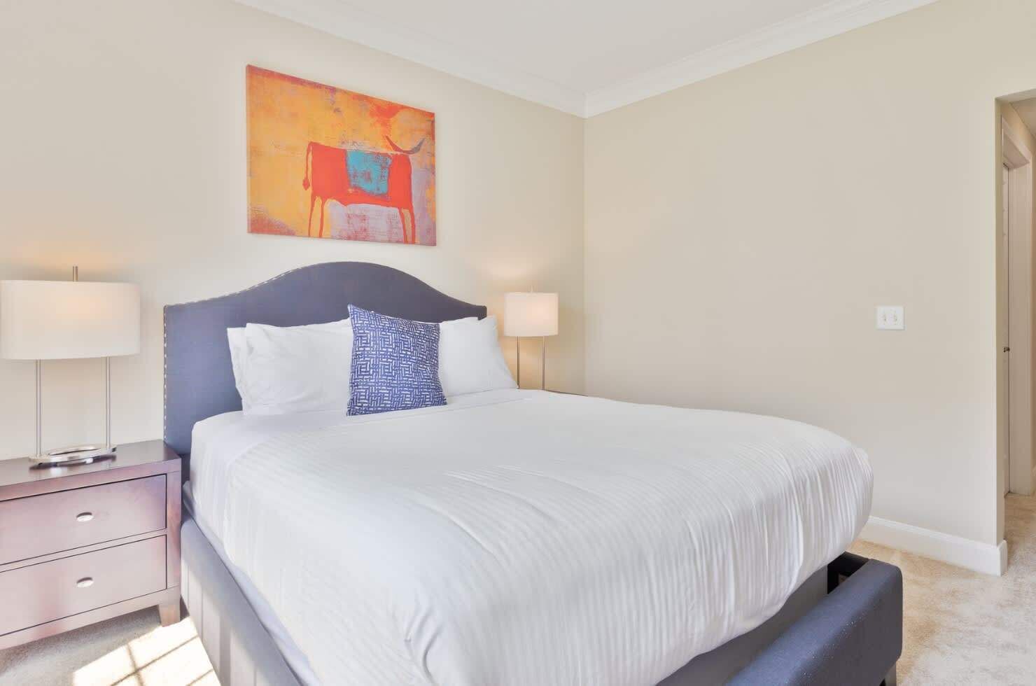A neatly arranged bedroom with a bed, two bedside tables, and a painting on the wall.