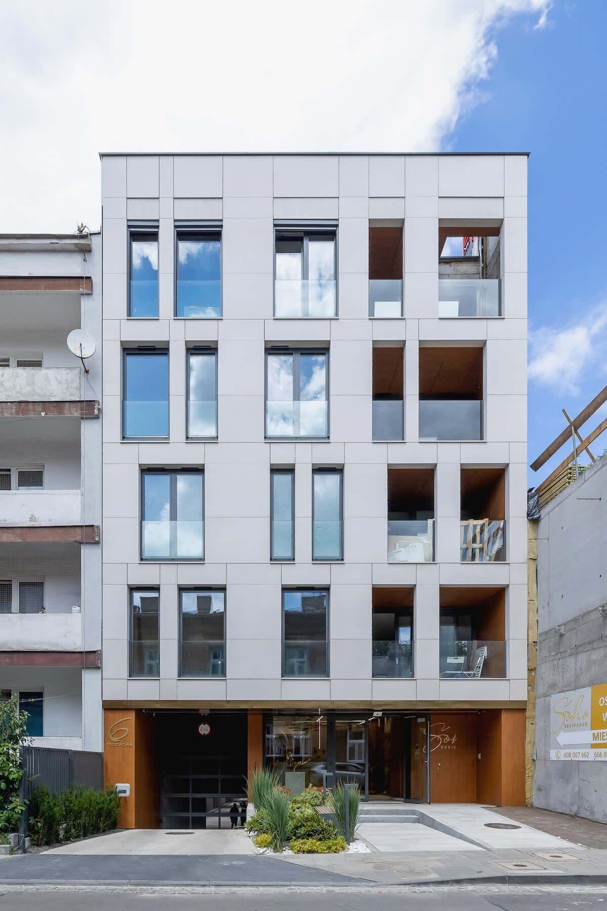 Ein modernes, mehrstöckiges Gebäude mit ebener Fassade, großen Fenstern und einem kleinen Vorgarten.