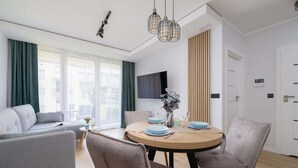 Una sala moderna con un sofá, una mesa de comedor para dos personas y un televisor montado en la pared.