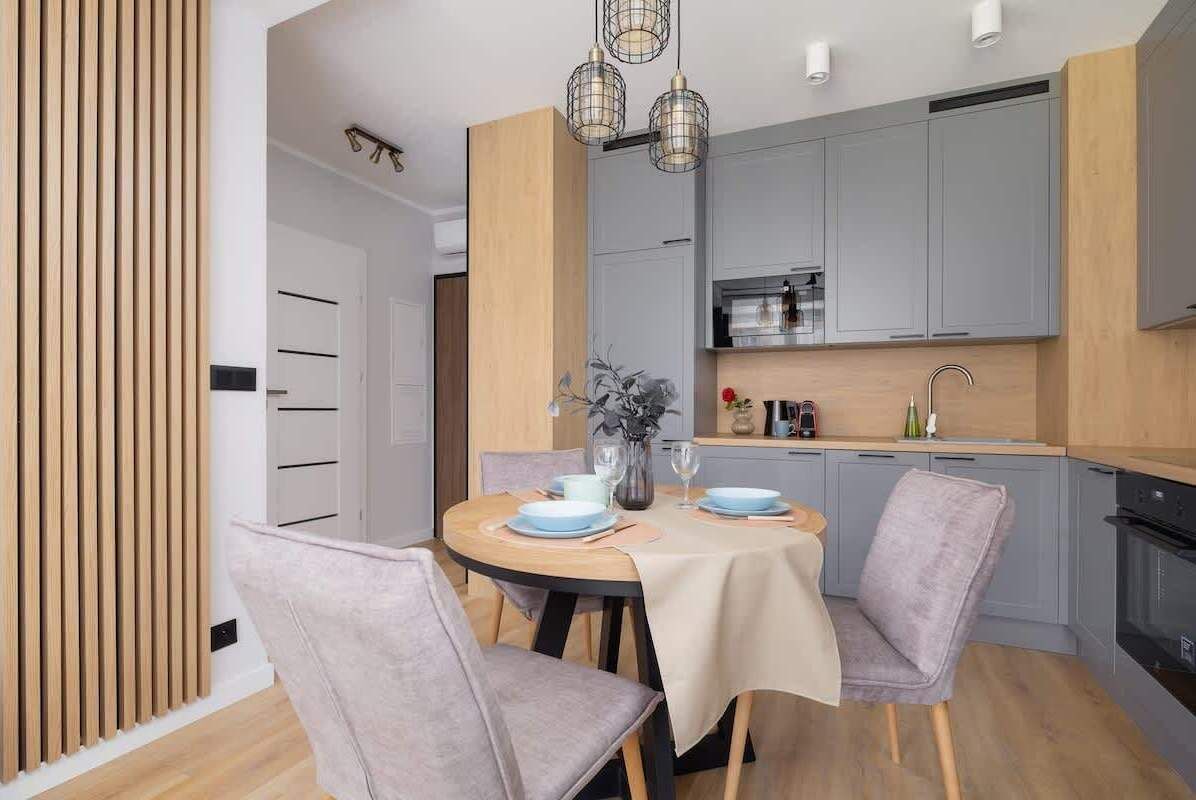 A modern kitchen with grey cabinets, a wooden countertop, and a dining area with a round table and two chairs.
