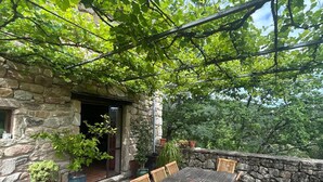 An outdoor patio with a wooden table and chairs, surrounded by stone walls and potted plants. - Self-contained, eco-renovated farmhouse in a small, unspoilt valley in the Cévennes. (Gagnières)
