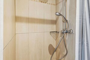 A shower with a handheld showerhead and a wall-mounted faucet.