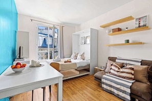 Una habitación moderna con cama, sofá, mesa de comedor con fruta y balcón con vistas.