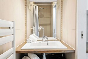 A bathroom with a white sink, a mirror, a shower, and a towel rack.