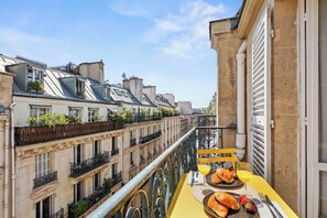 A balcony with a yellow table set for breakfast, overlooking a cityscape with historic buildings.