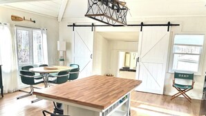 A kitchen with a wooden island, a dining area with green chairs, and a view through a sliding door.
