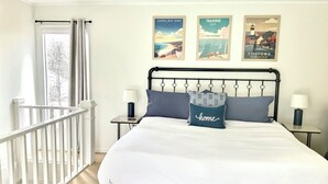 A bedroom with a bed, two bedside tables, a window with curtains, and three framed pictures on the wall.