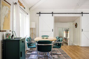 Un comedor con una mesa redonda, seis sillas, un mantel a cuadros y un armario de madera.