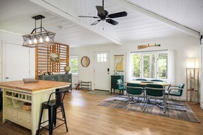 Una habitación amplia con una mesa de comedor de madera, sillas verdes, un ventilador de techo y un gran ventanal con vistas al exterior.