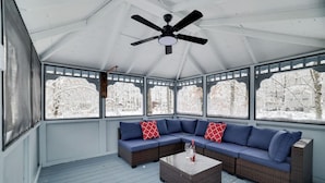 A covered patio with a sectional sofa, a coffee table, and large windows offering a view of a snowy landscape.