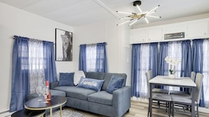 A modern living room with a grey sofa, a round coffee table, and a dining area with a white table and grey chairs.