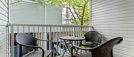 A balcony with wicker furniture and a view of a building with white siding.
