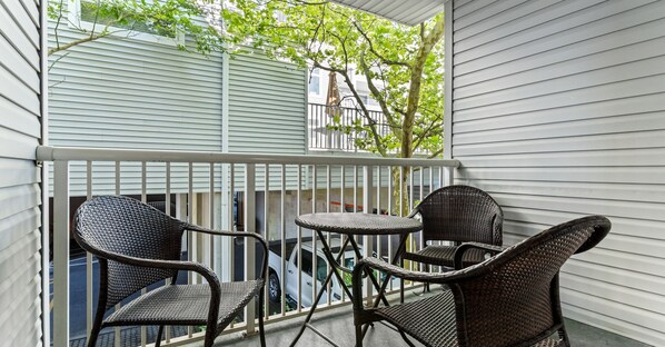 A balcony with wicker furniture and a view of a building with white siding.