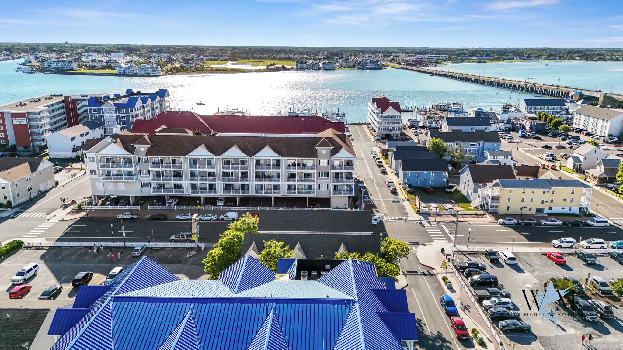 A coastal hotel with a central building featuring balconies and a parking lot in front.