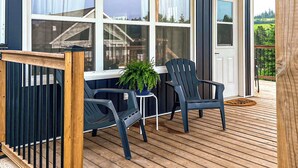 Un porche cubierto con dos sillas Adirondack, una planta en maceta y barandilla de madera para la terraza.