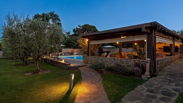 A covered outdoor patio with stone walls, a swimming pool, and a stone pathway.