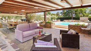 An outdoor patio with a pool, a sofa, wicker furniture, and a dining area with chairs and a table. - Villa Castiglione 9 Emma Villas (Castiglione della Pescaia)