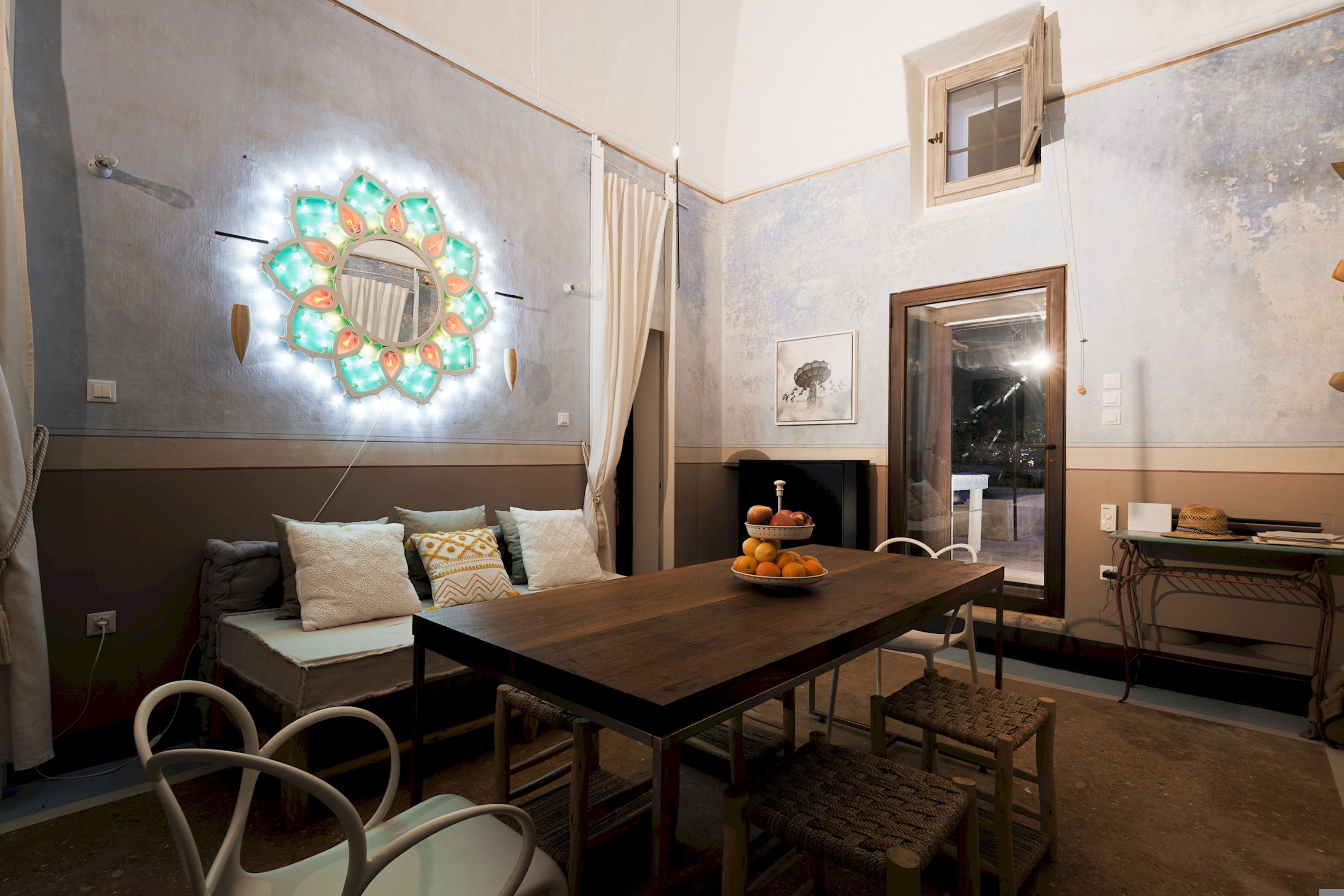 A dining area with a wooden table, chairs, a decorative wall light, and a sofa with cushions.