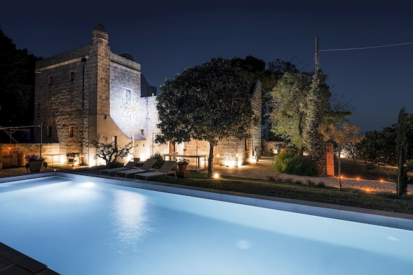A swimming pool with lounge chairs, a stone building with a tower, and trees. - Masseria Muto 6 Emma Villas (Ruffano)