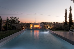 A swimming pool with a stone wall and a fire feature in the background. - Masseria Muto 6 Emma Villas (Ruffano)