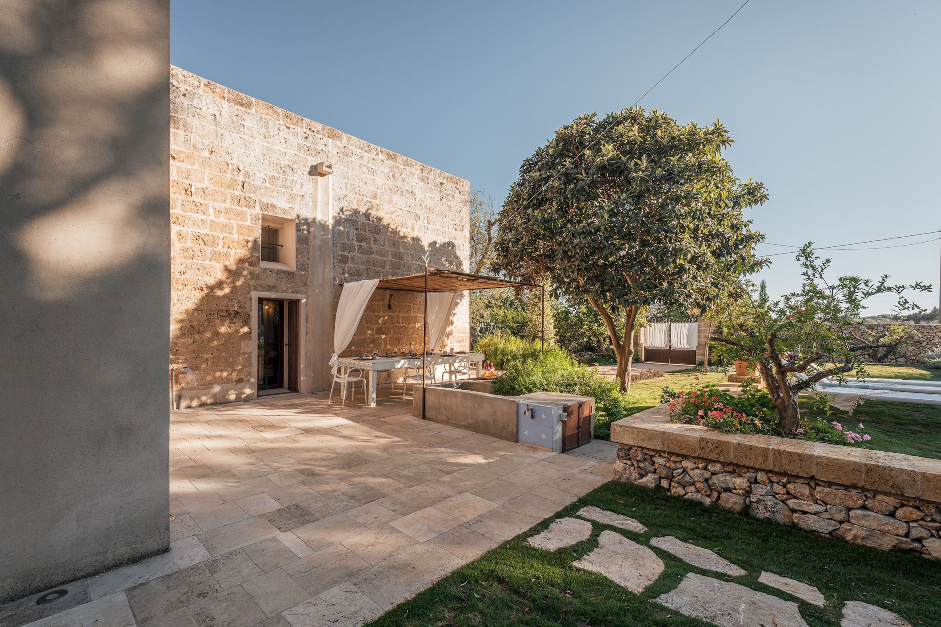 A stone building with a patio area, outdoor furniture, and a tree.