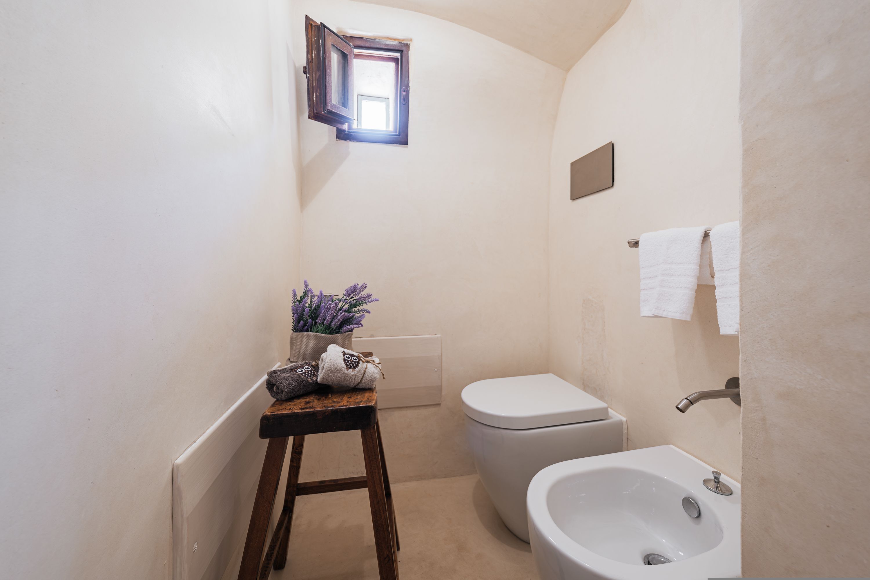 A compact bathroom with a toilet, sink, and a small stool with decorative items.