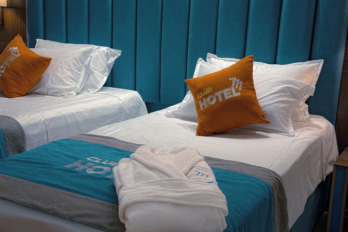 Two twin beds with matching pillows, a blue headboard, and a towel on the bed.