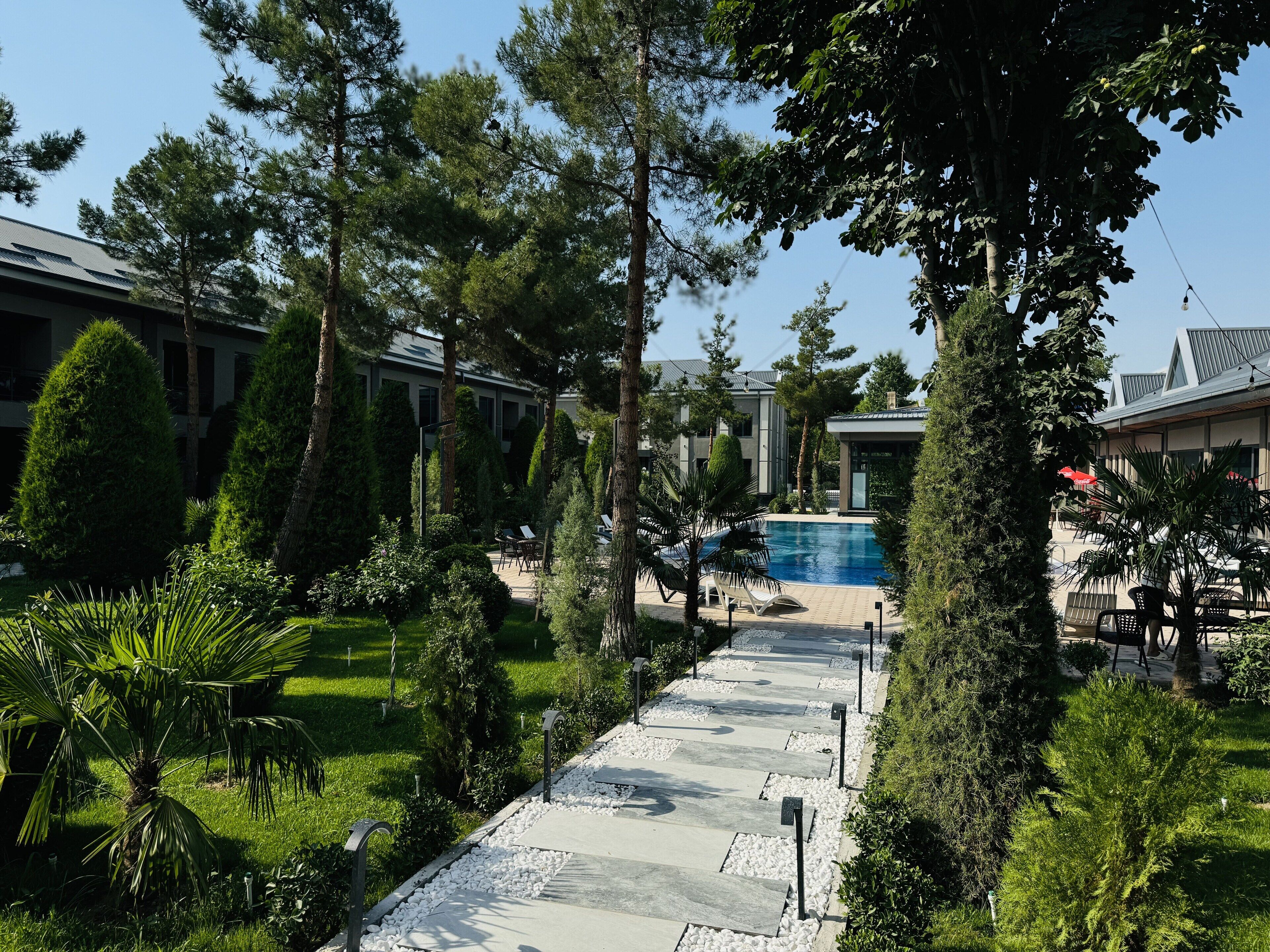 A pool area with lounge chairs, surrounded by trees and a pathway.