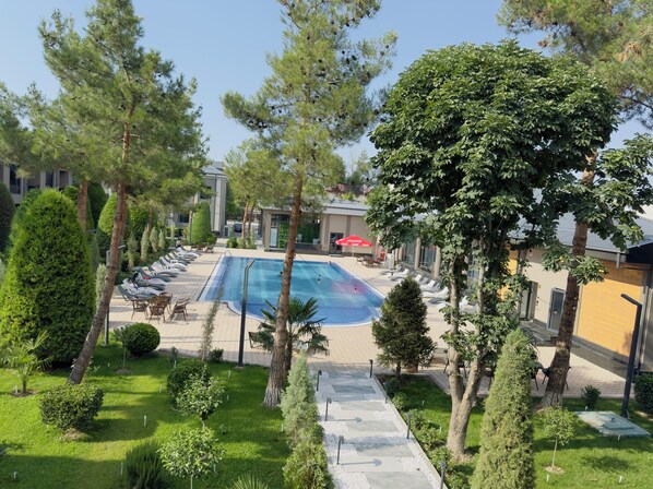 Un espace piscine avec des chaises longues et une piscine entourée d’arbres et d’un bâtiment.